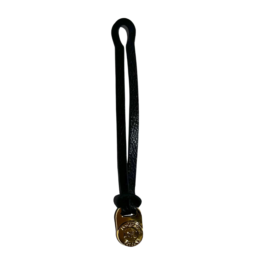 Black leather bag charm with a gold-tone medallion on a white background