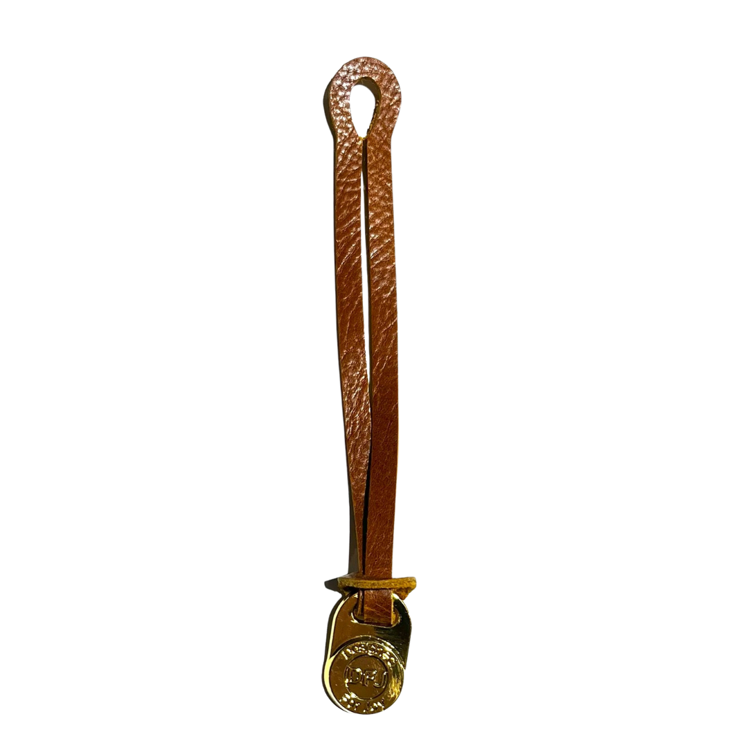Caramel brown leather bag charm with a gold-tone medallion on a white background