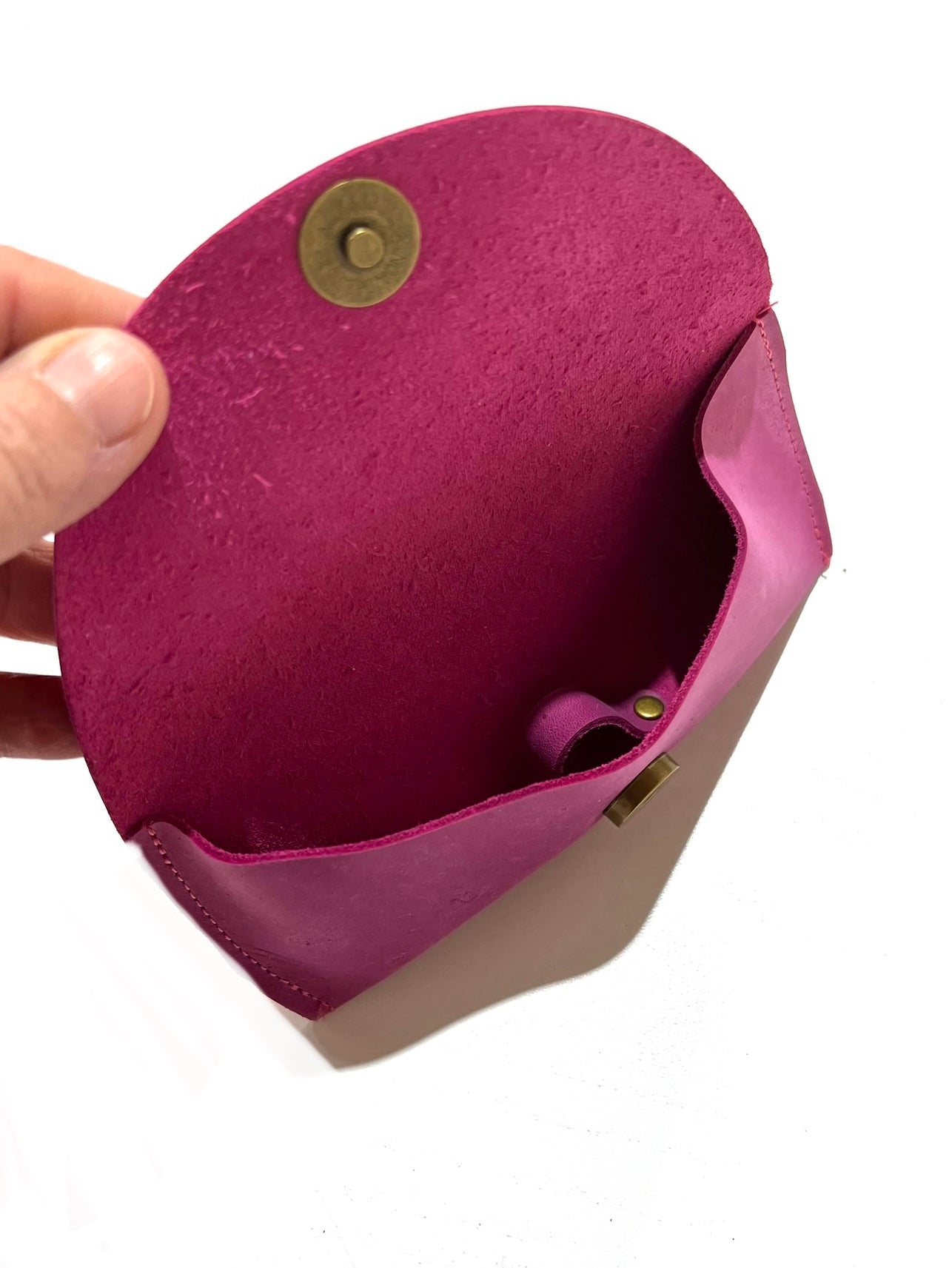 Inside a raspberry pink leather sunglasses case with a hand holding it open, displayed on a white background