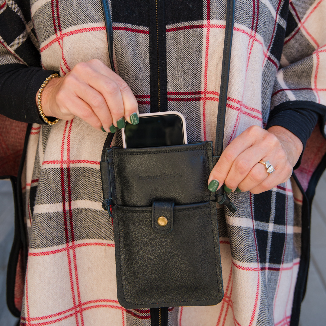 Close-up of a person wearing a black mini crossbody handbag while pulling a phone out of it