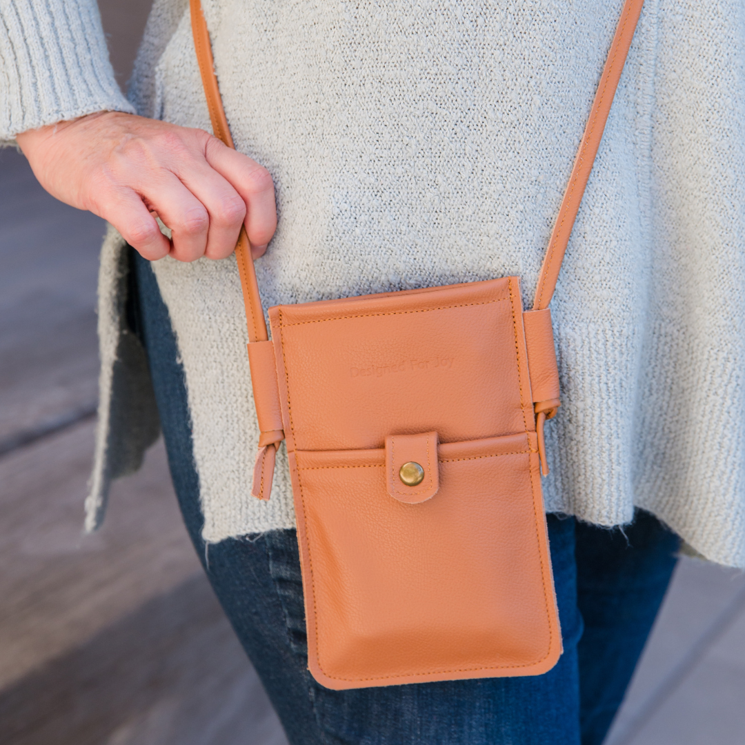 Close-up of a person wearing a caramel brown mini crossbody handbag in an outdoor setting