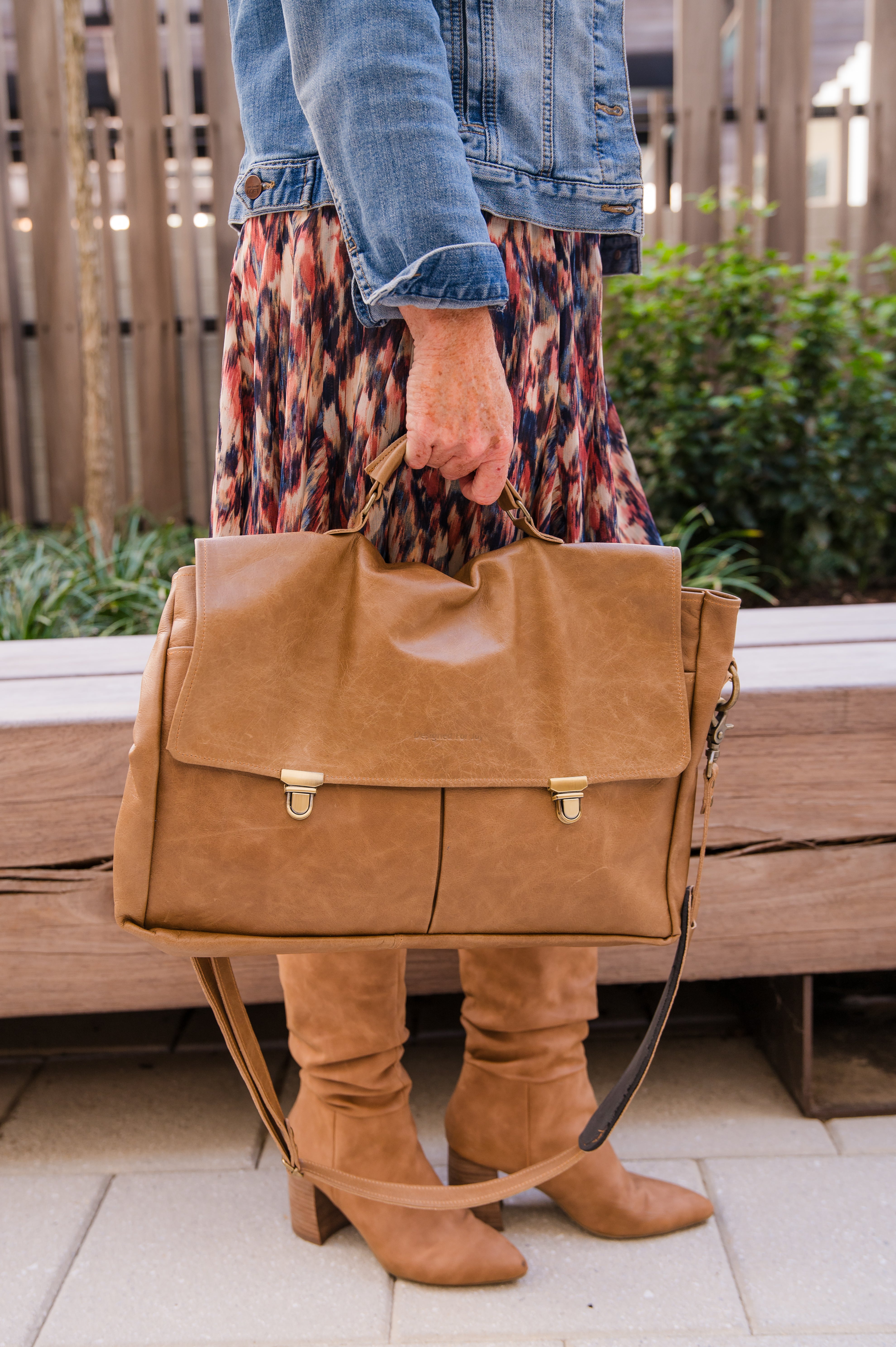 Person holding a caramel brown professional messenger/laptop bag in an outdoor setting
