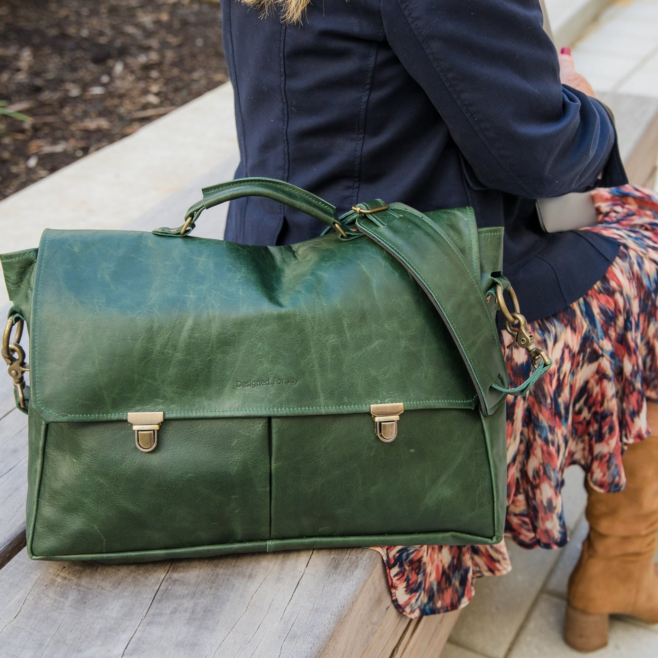Person sitting next to a dark green professional messenger/laptop bag in an outdoor setting