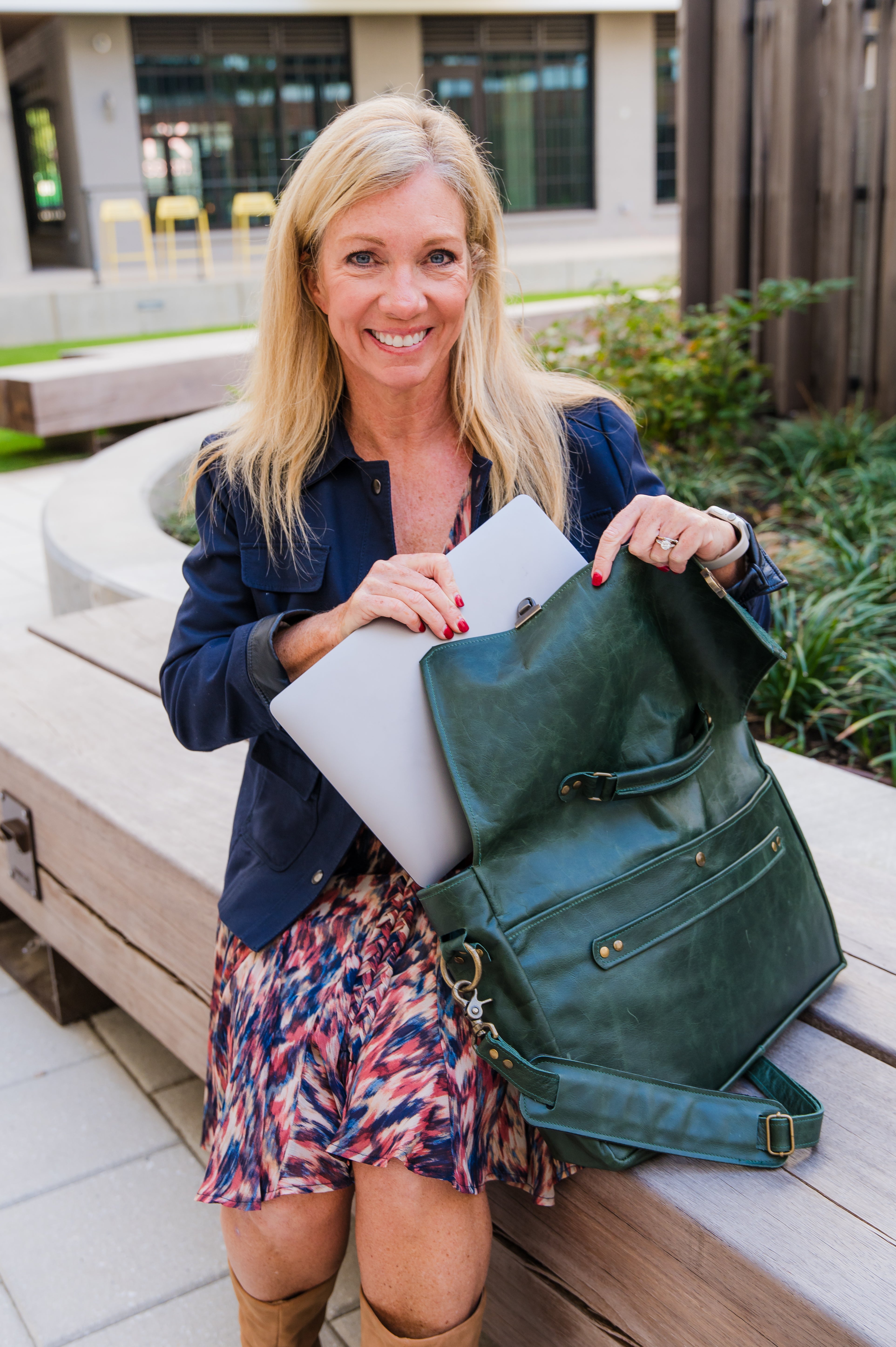 Women smiling while putting a laptop into a dark green professional messenger/laptop bag in an outdoor setting