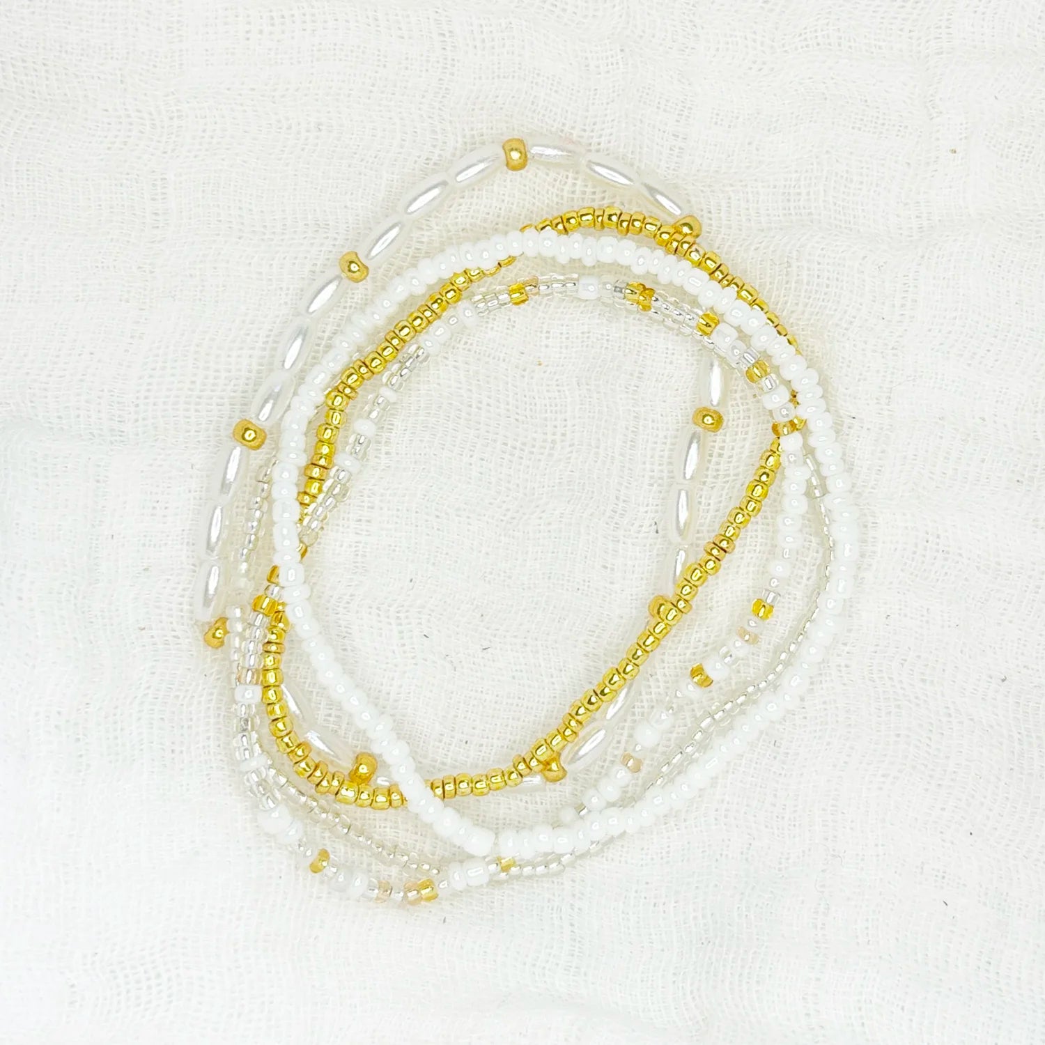 Stackable bracelet with neutral seed, gold, and silver beads, displayed on a white fabric background