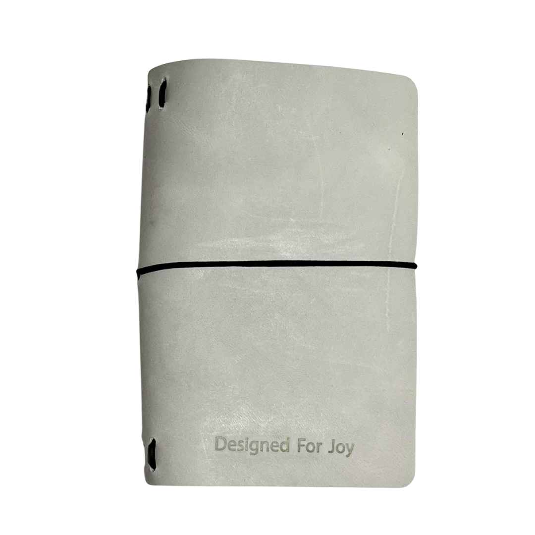 Light gray notebook with 'Designed for Joy' text on the cover and a black strap, on a white background