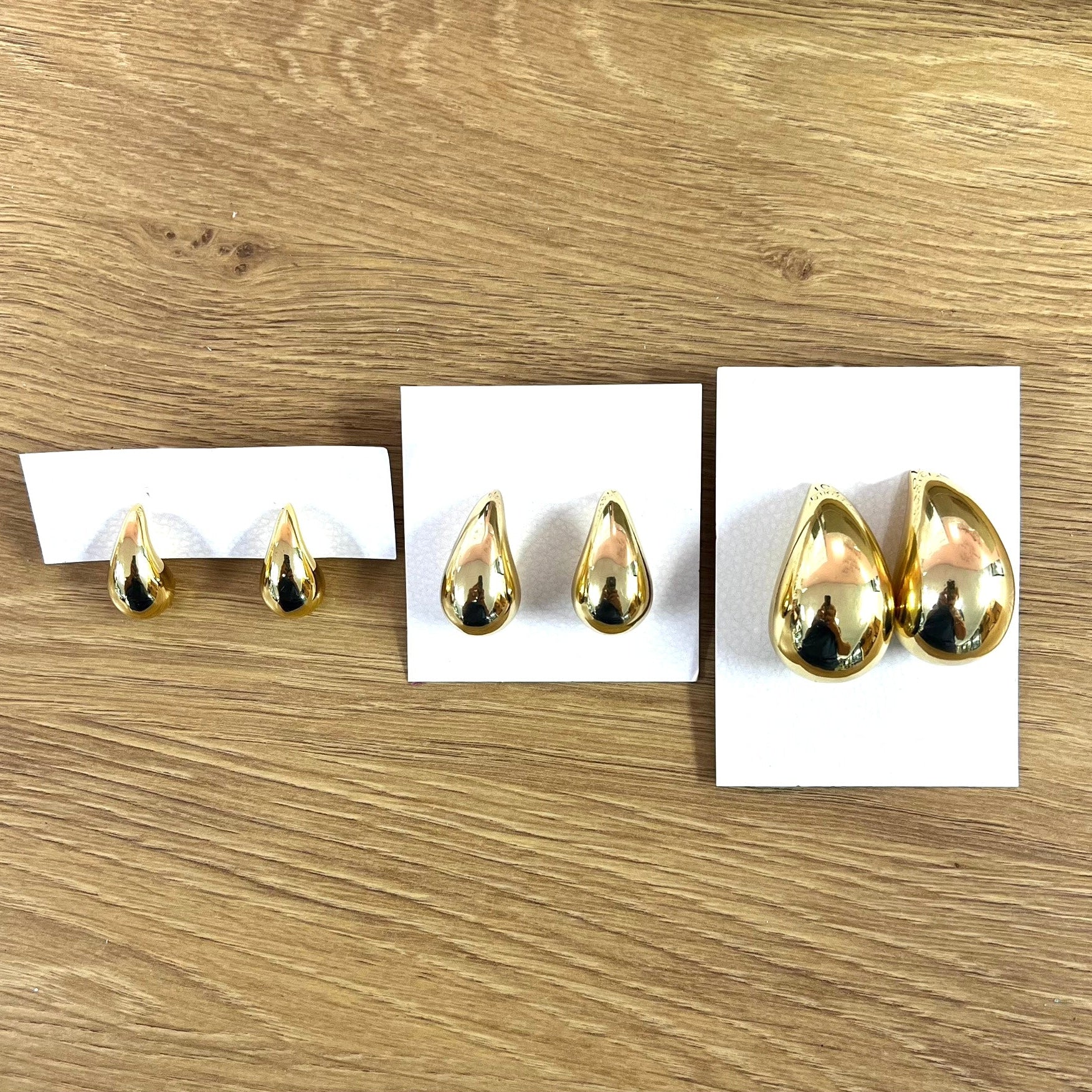 Three pairs of gold puffy teardrop earrings in the sizes small, medium, and large, on a wooden background