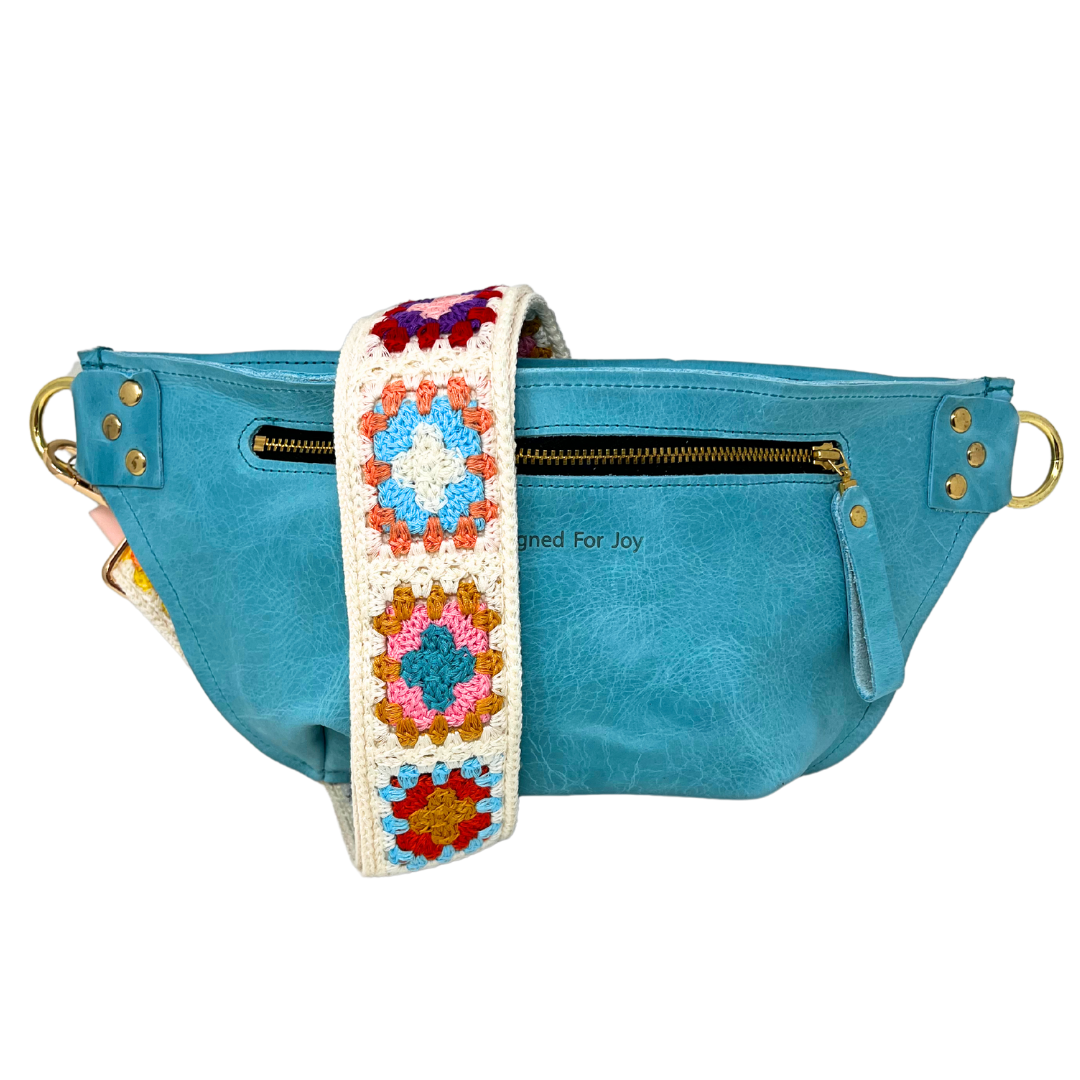 Aqua blue leather crossbody sling bag with a multicolored crochet square strap, featuring a full zippered compartment