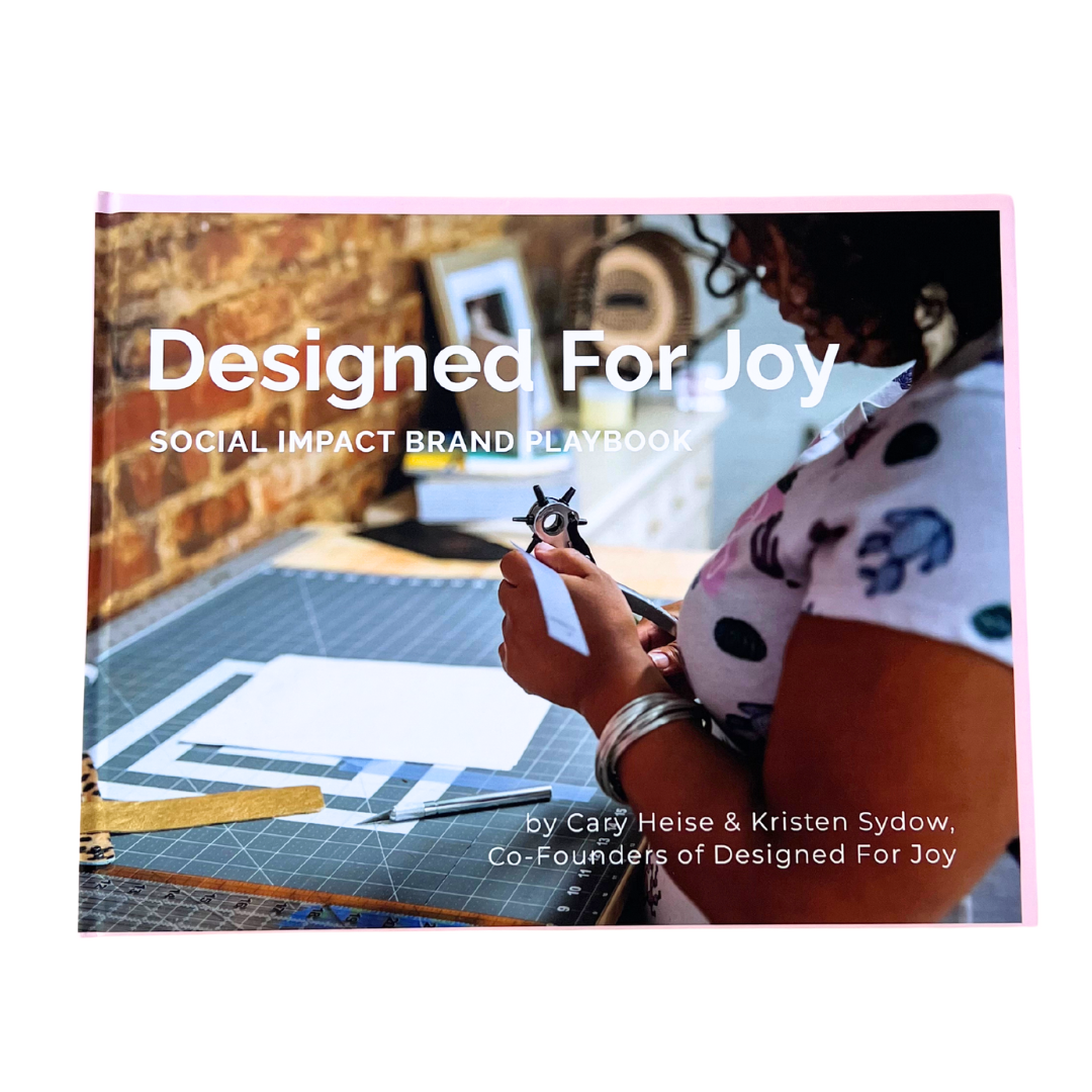 Book called 'Designed For Joy Social Impact Brand Playbook' that has an image of person working with tools
