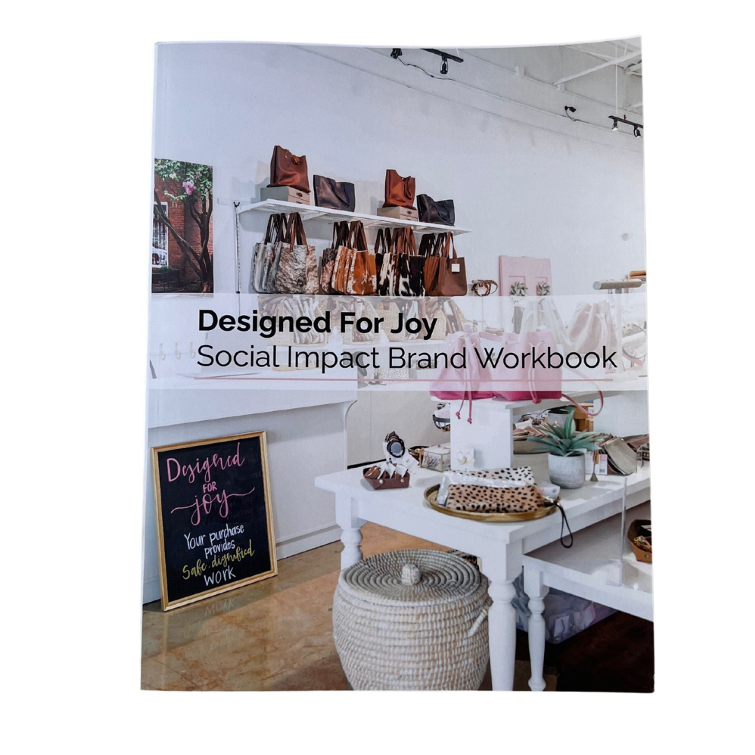 Book called 'Designed for Joy Social Impact Brand Workbook' with a photo of the inside of the boutique