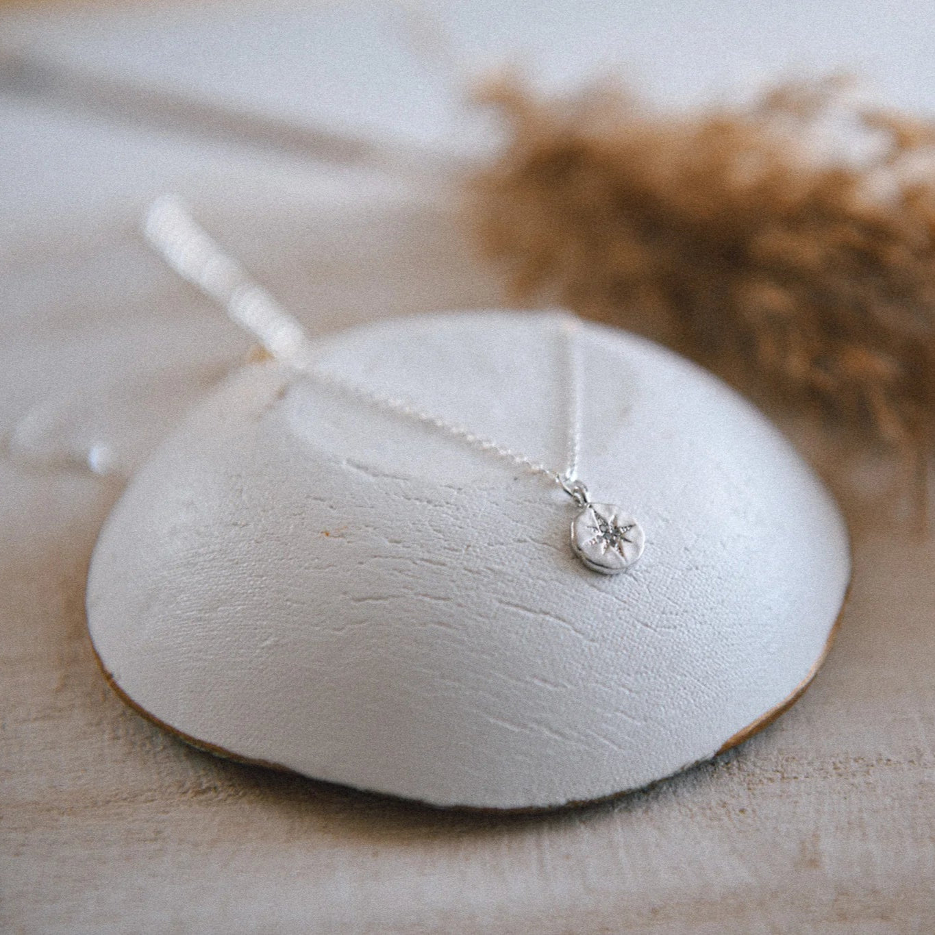 Silver necklace with a compass pendant, displayed on a white stone against a blurred background