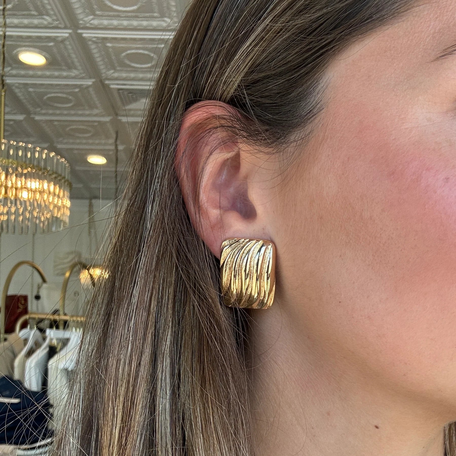 Close-up of a person wearing a gold-colored rectangular stud earring