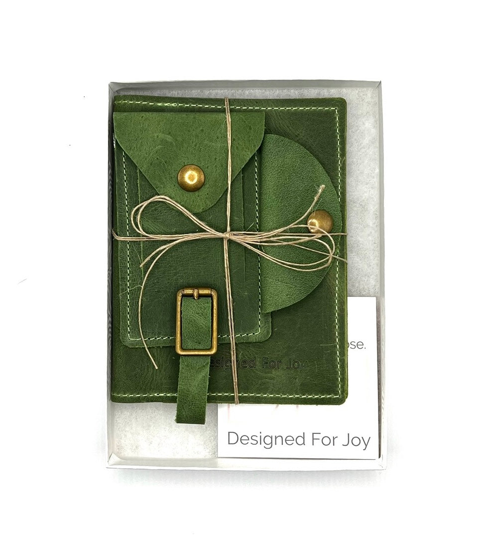 Evergreen leather travel bundle including a passport cover, a cord organizer, and a luggage tag, packaged for gifting with a card that reads 'Designed For Joy'