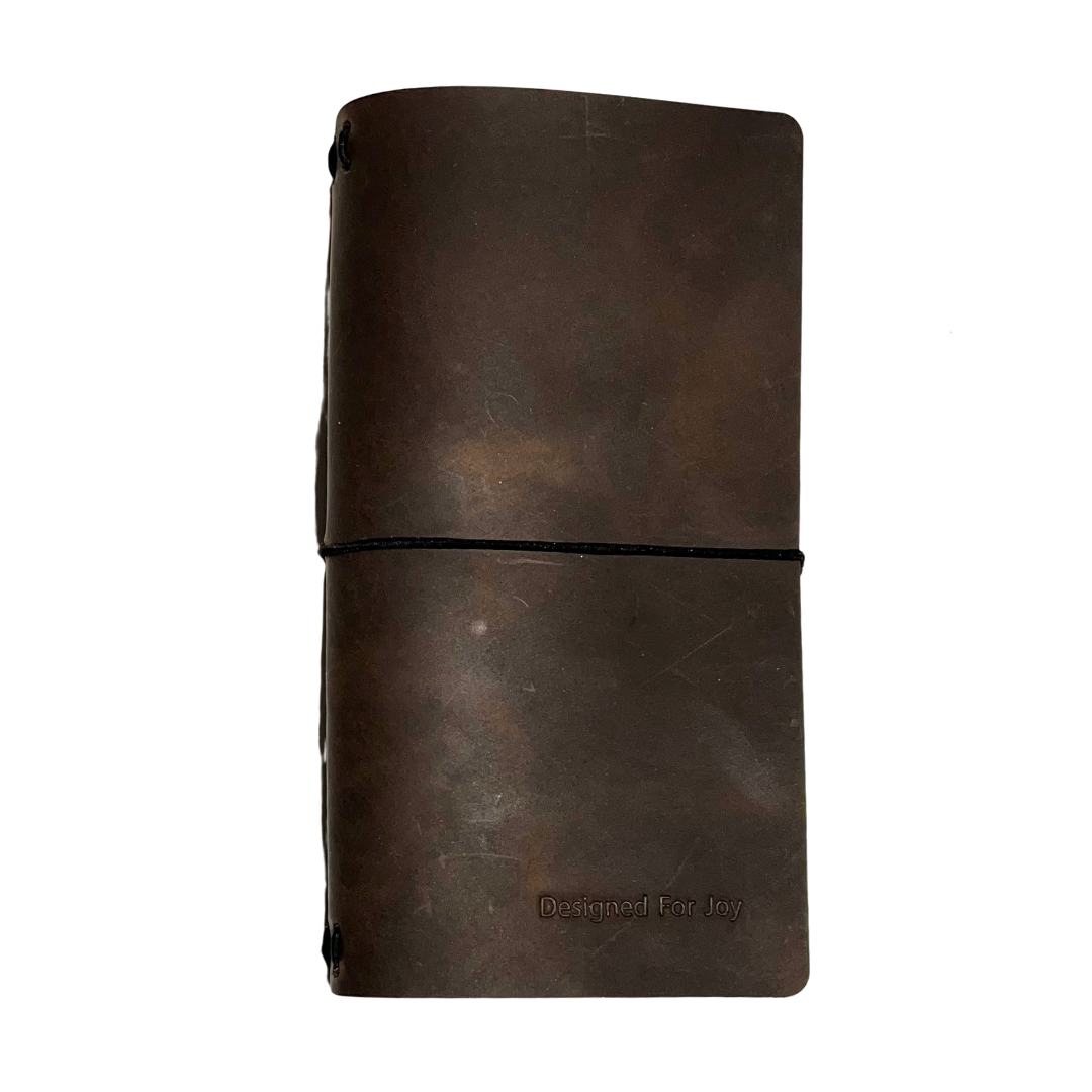 Brown notebook with a black strap and 'Designed for Joy' text, on a white background