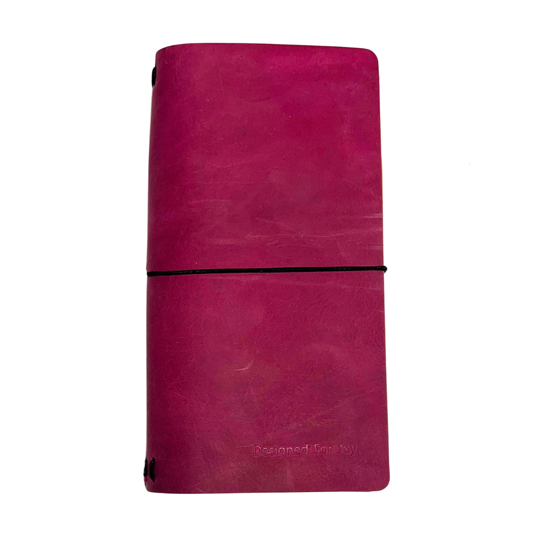 Pink notebook with a black strap and 'Designed for Joy' text, on a white background