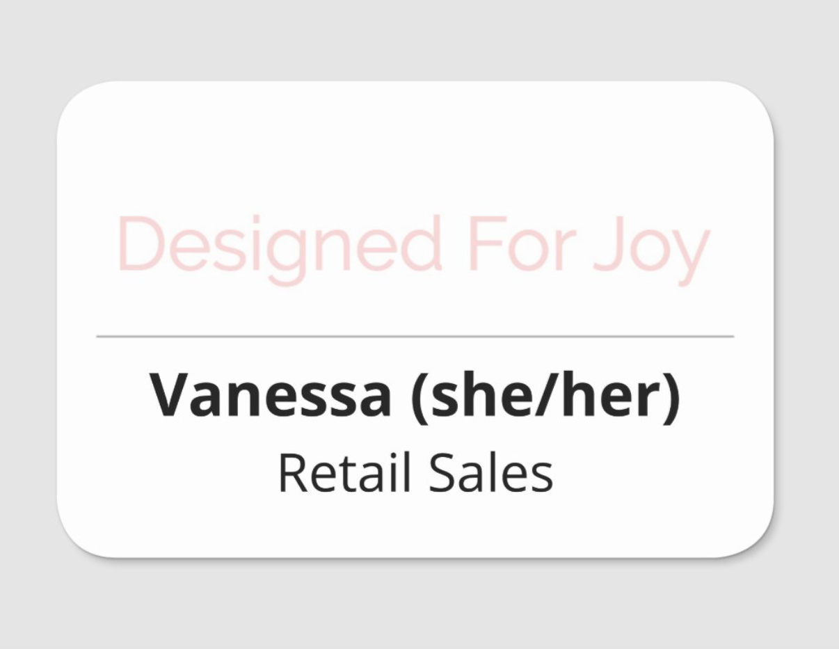 White name tag with 'Designed For Joy' text on the top and 'Vanessa (she/her) Retail Sales' on the bottom