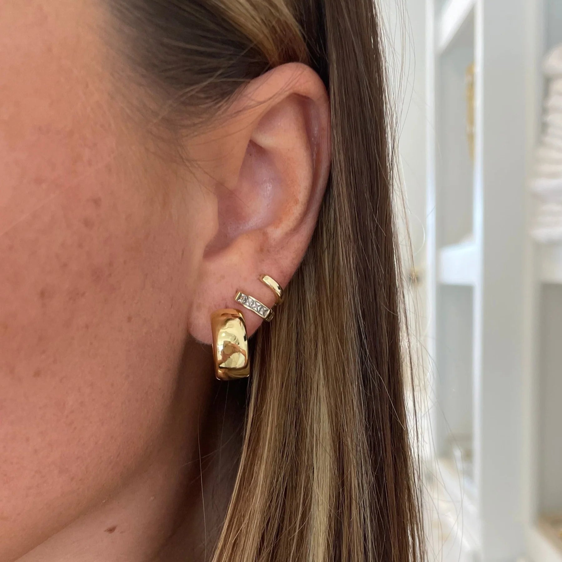 Person wearing a gold-colored wide mini hoop earring