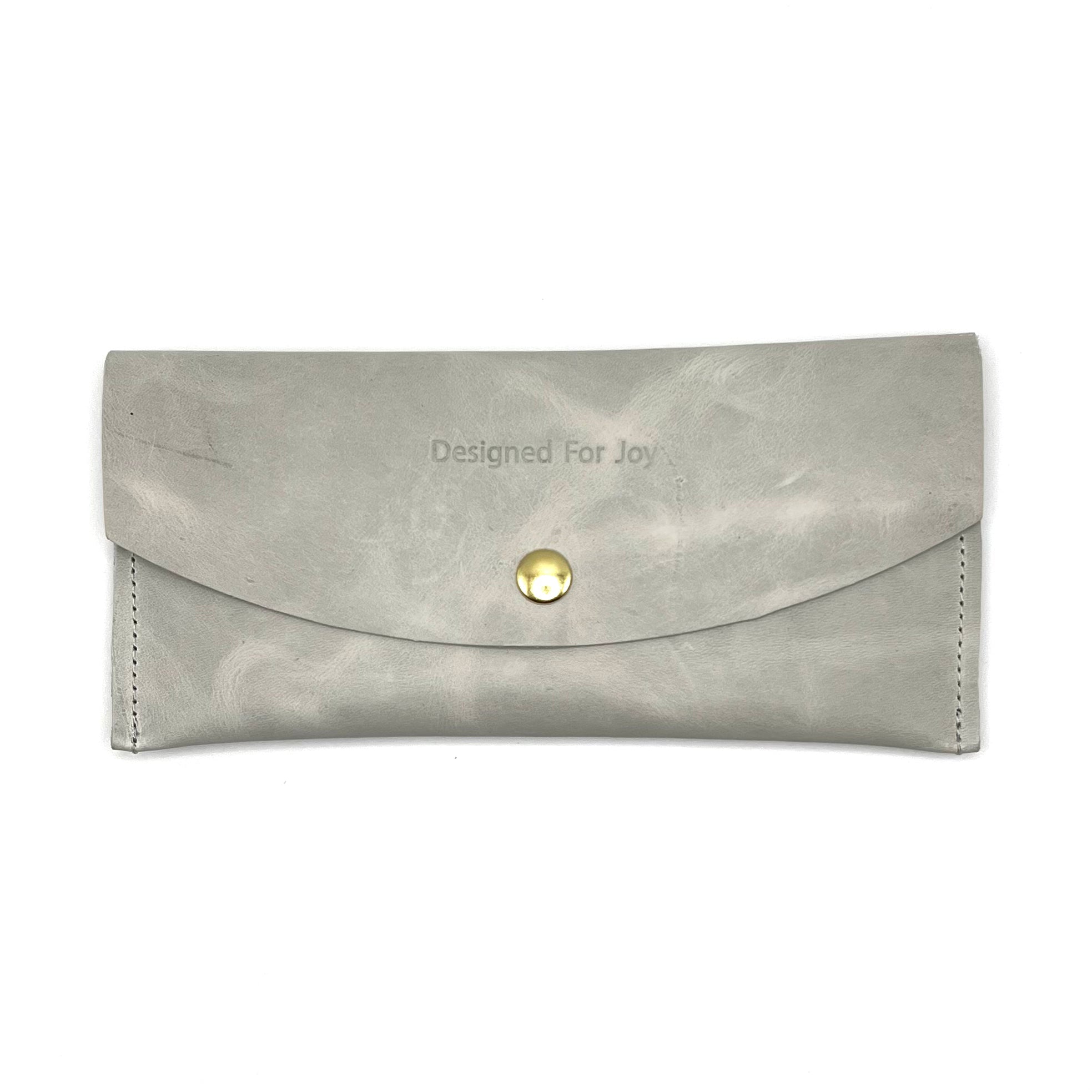 Gray leather penny wallet with snap closure and 'Designed for Joy' text, displayed on a white background