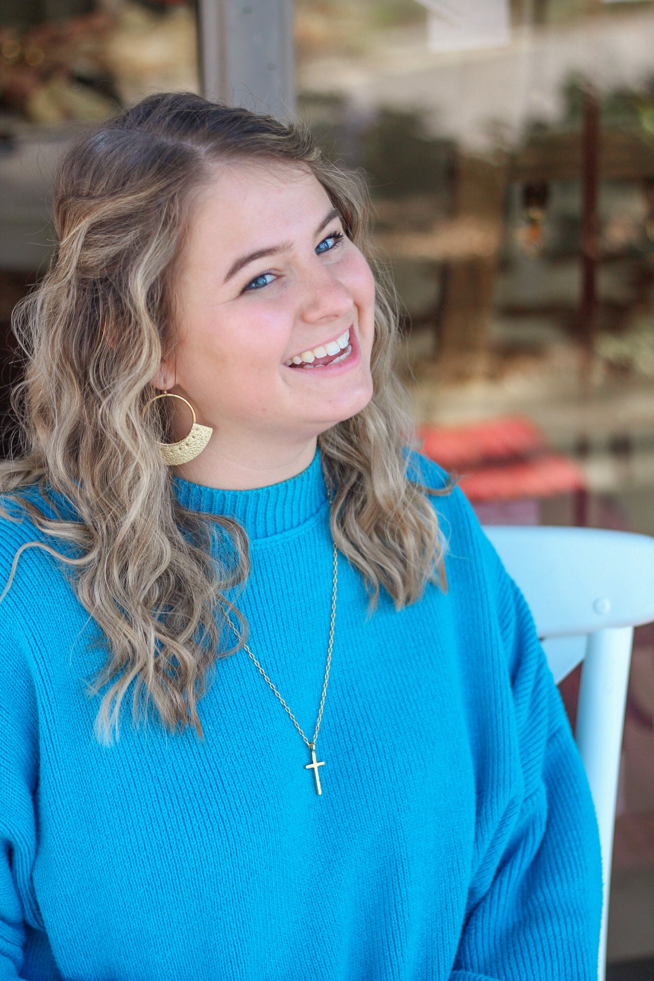 A person wearing a gold cross necklace while in an outdoor setting