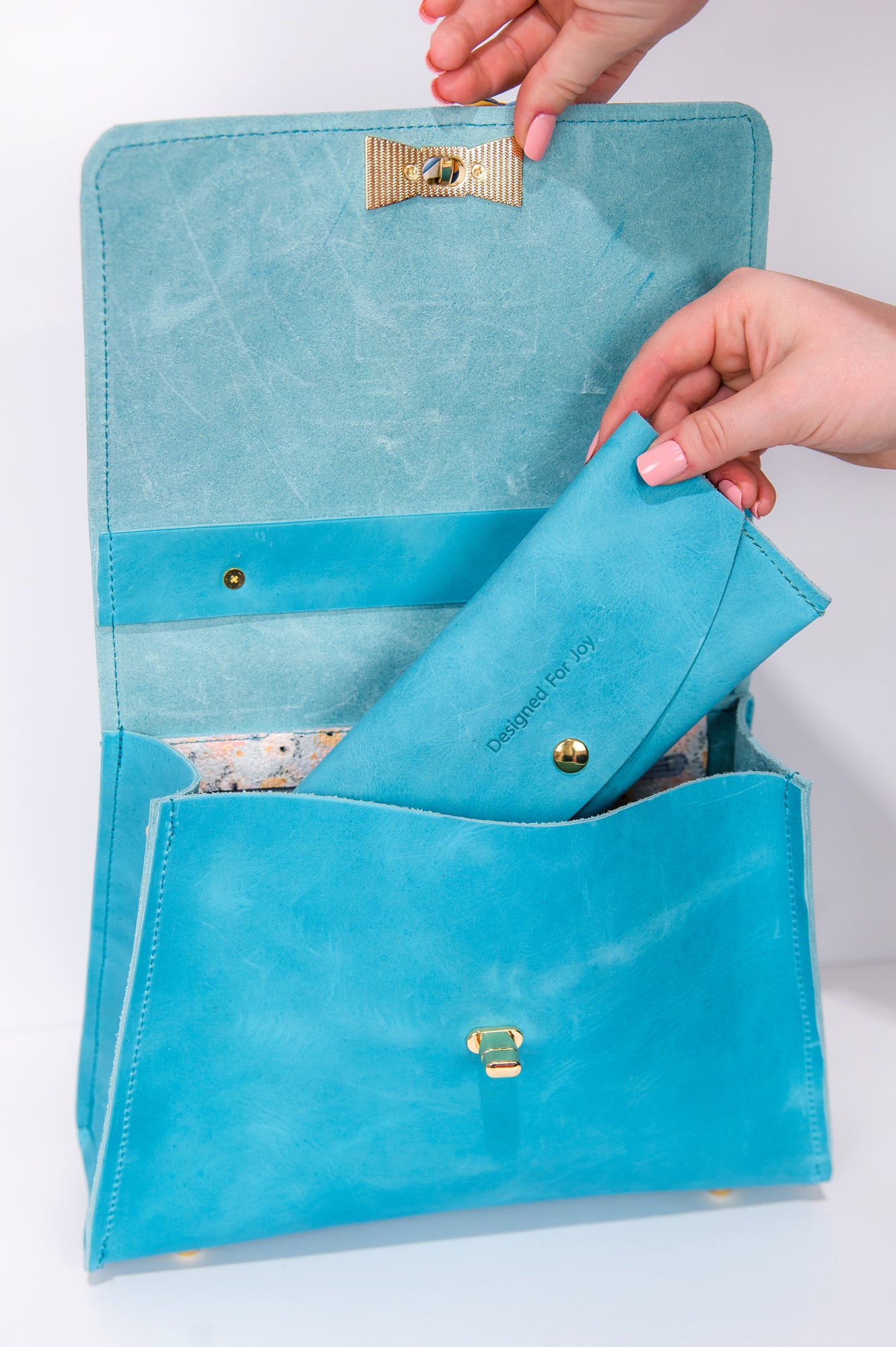 Hands putting an aqua blue penny wallet into an aqua blue bag
