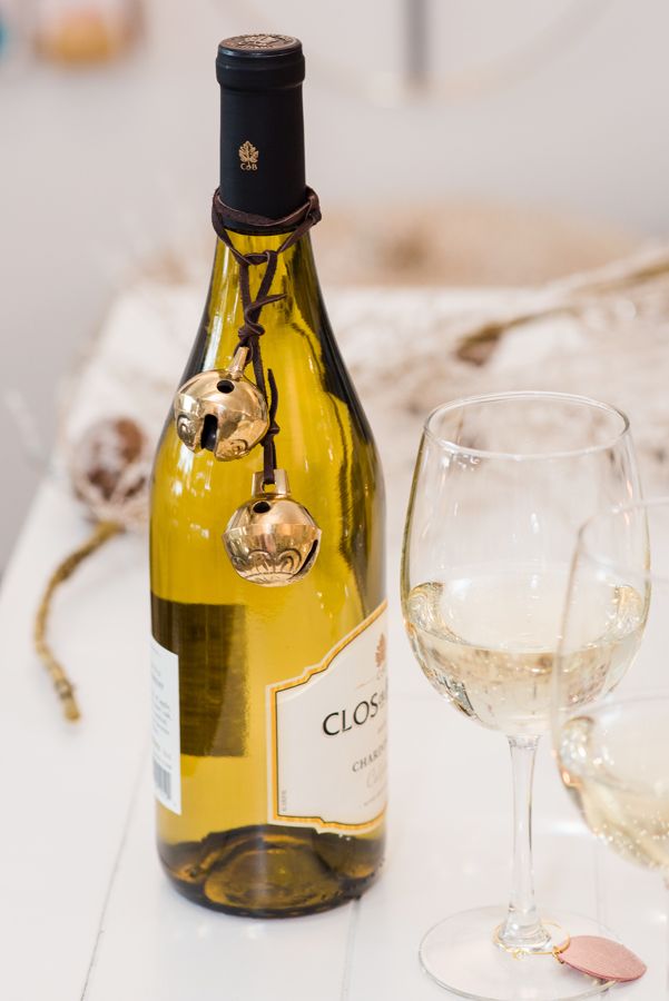 A jingle bell embellishment tied around a wine bottle, next to a wine glass