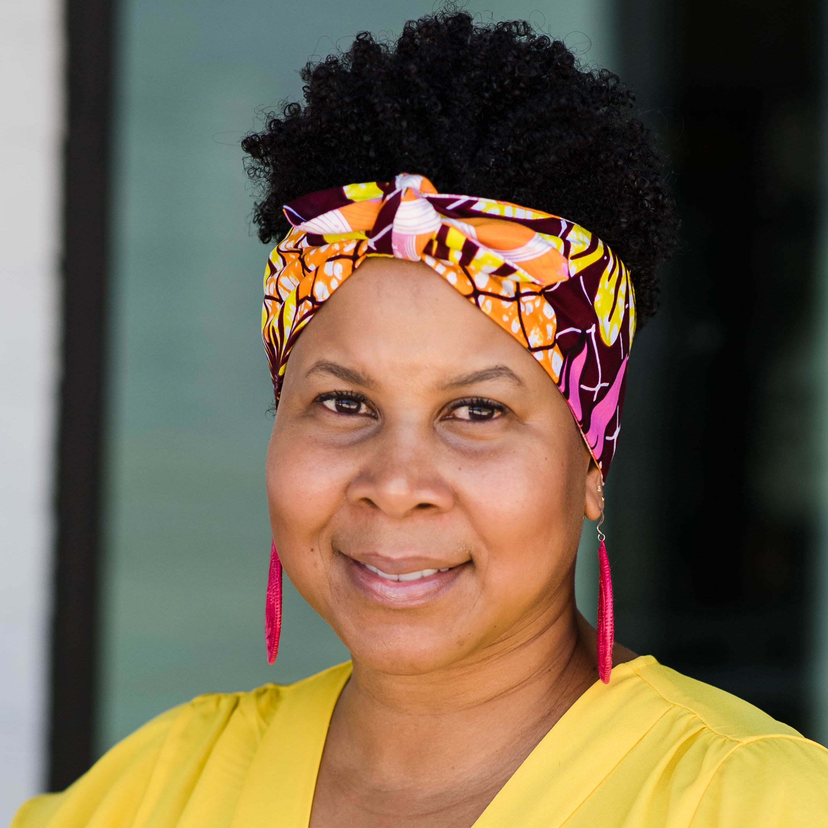 A person smiling while wearing an orange and yellow head wrap
