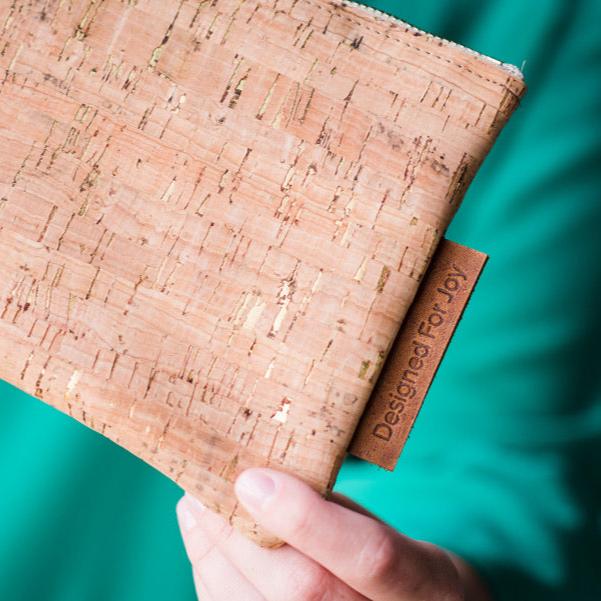 Close-up of a person holding a cork wristlet that has a leather tag labeled 'Designed for Joy'