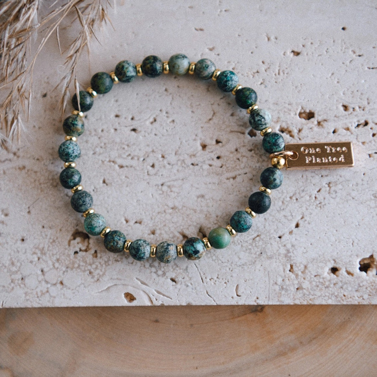 African turquoise beaded bracelet with gold colored spacer beads and a tag with 'One Tree Planted' text, displayed on a stone surface