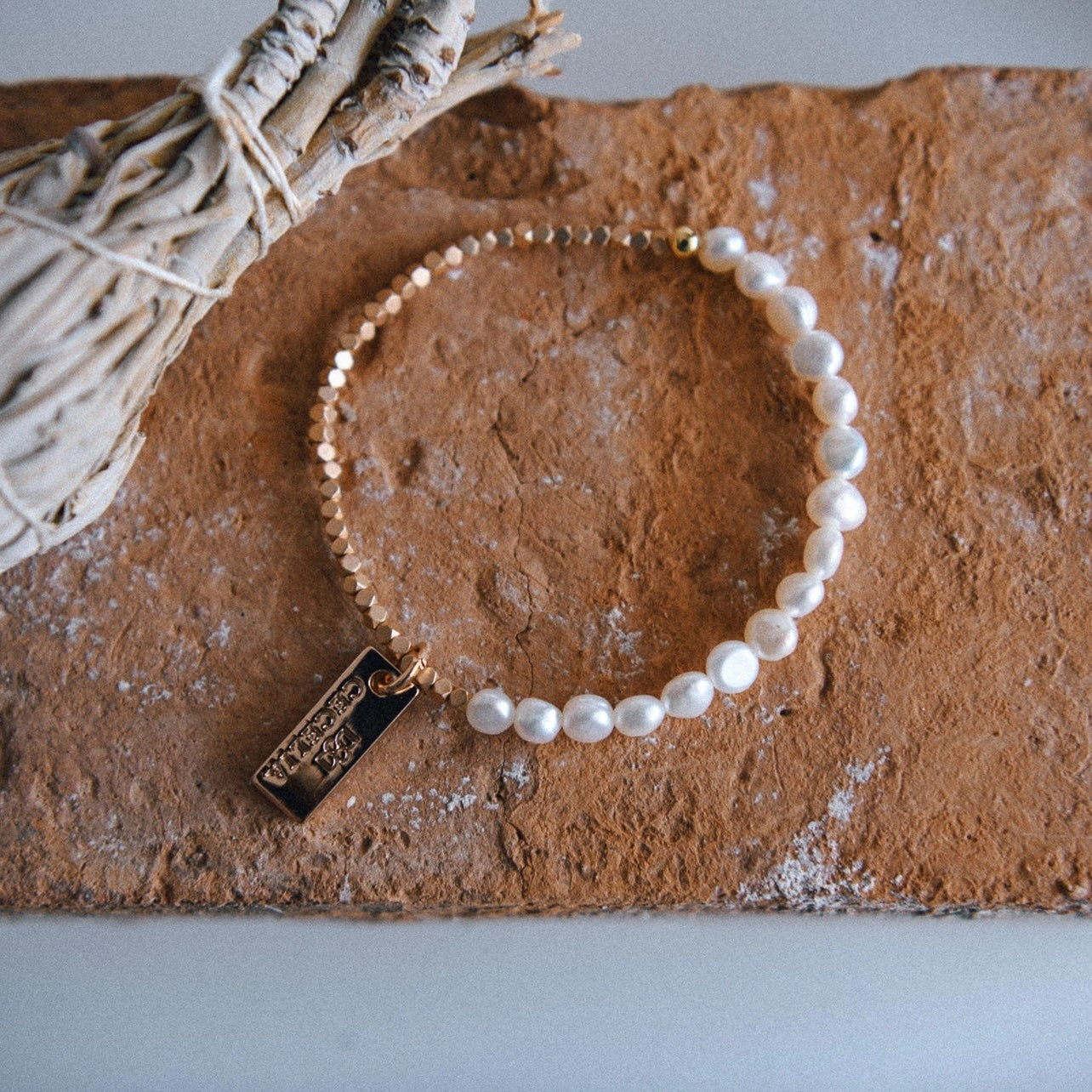 Half freshwater pearl, half matte gold bead bracelet on a stone surface next to a bundle of sage