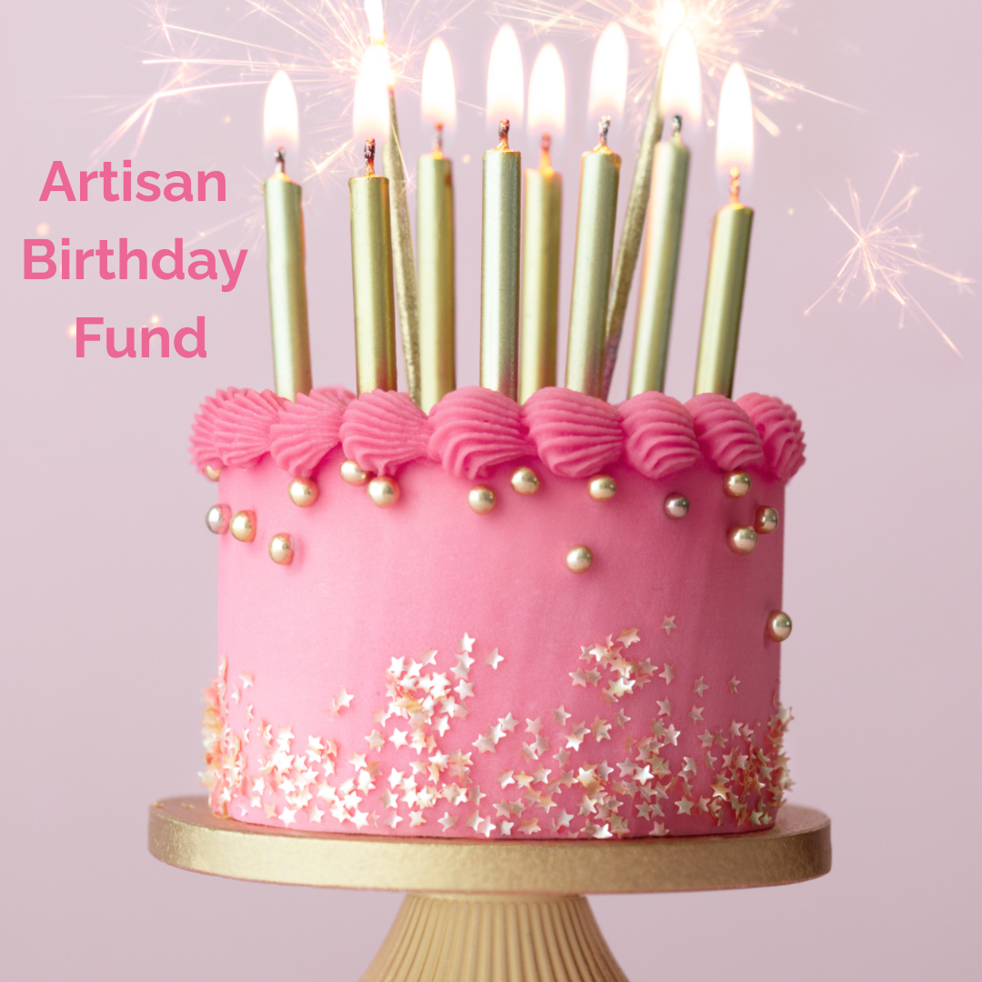 Pink birthday cake with lit candles on a gold cake stand against a light purple background with the text 'Artisan Birthday Fund'
