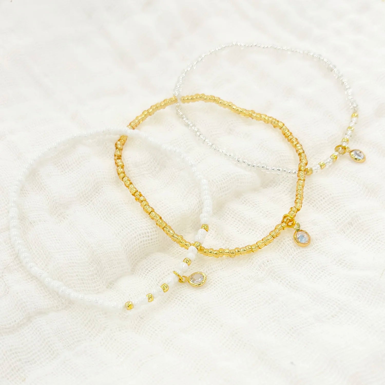 Three seed beaded bracelets in various colors, displayed on a white fabric background