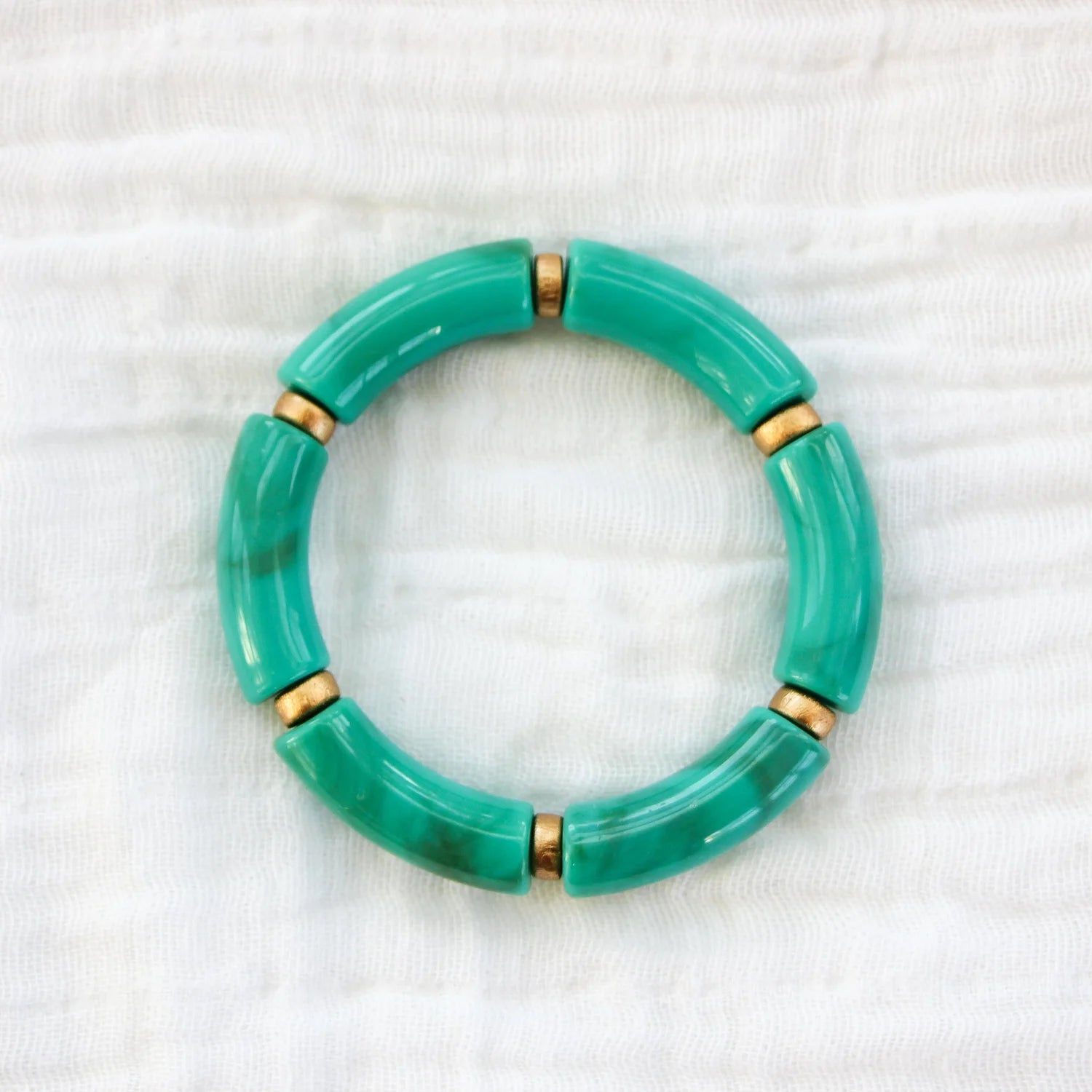 Bracelet featuring turquoise acrylic beads with gold spacers, displayed on a white fabric background