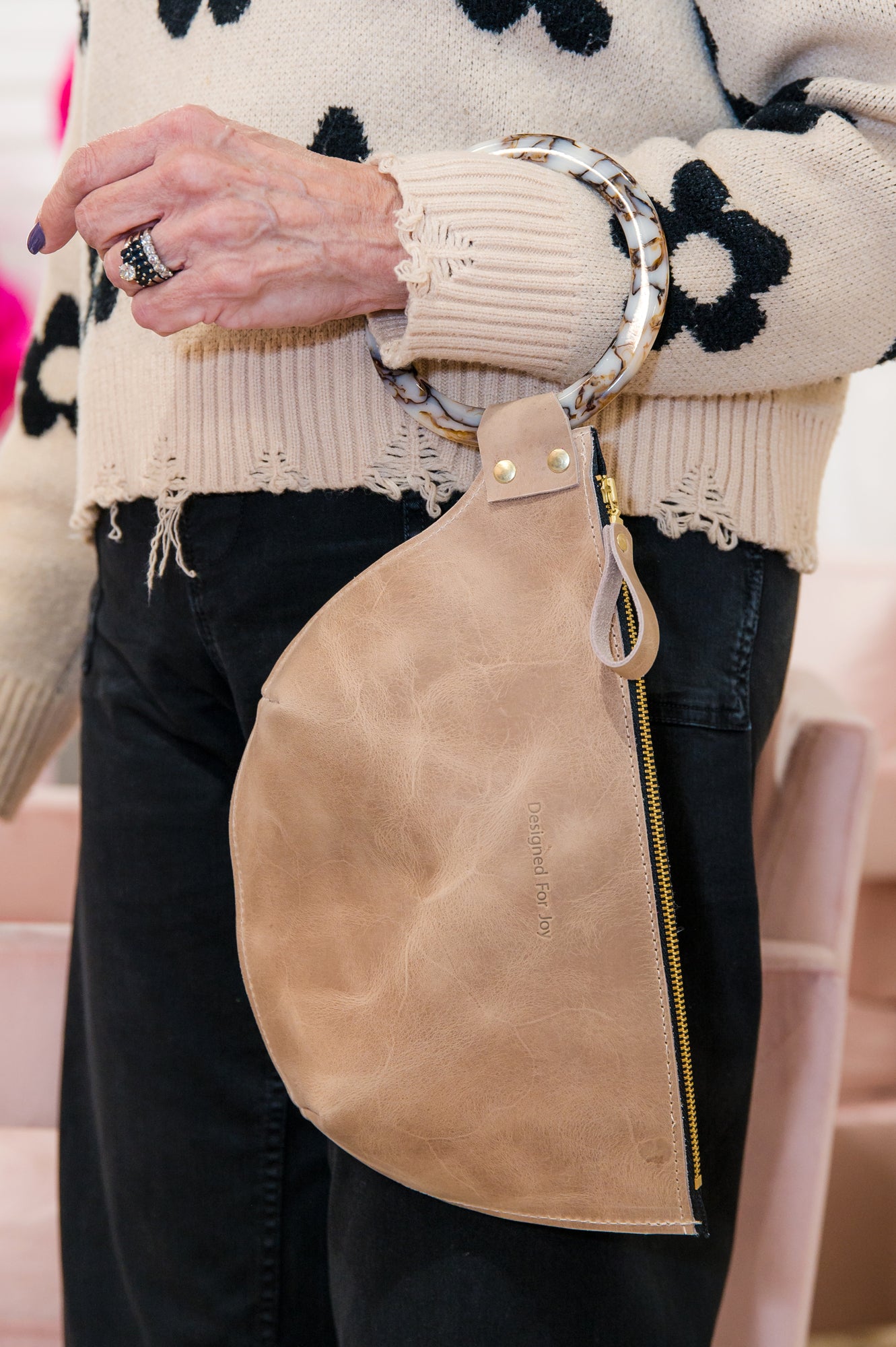 Close-up of a person wearing a tan wristlet handbag on their arm